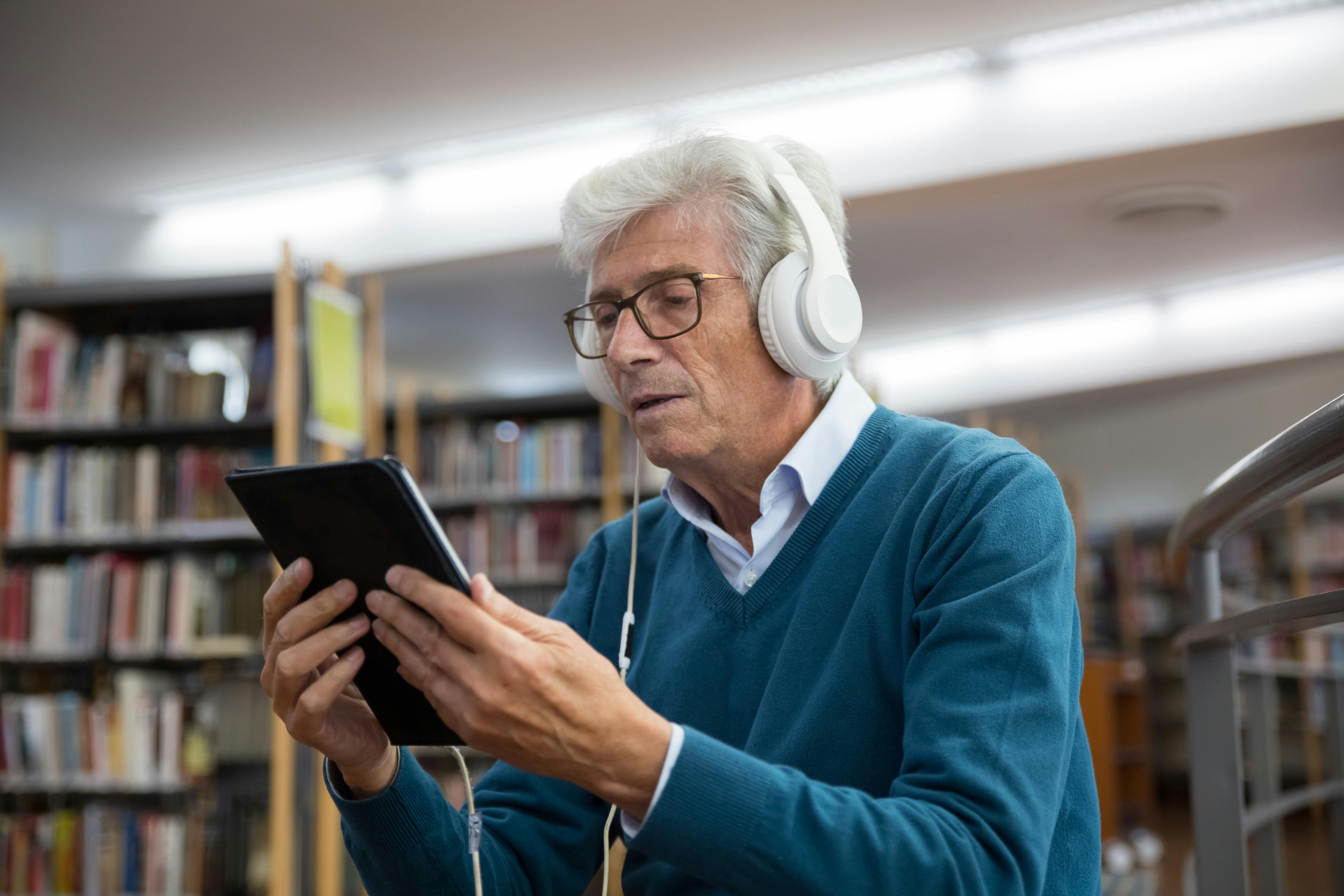 Image of elderly man reading in a library using a tablet